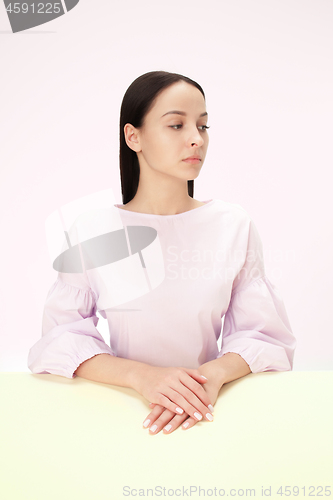 Image of Serious business woman sitting at a table on a pink background