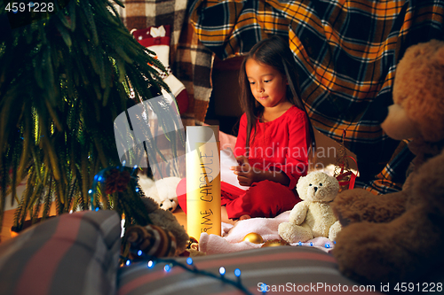 Image of Merry Christmas and Happy Holidays. Cute little child girl writes the letter to Santa Claus near Christmas tree