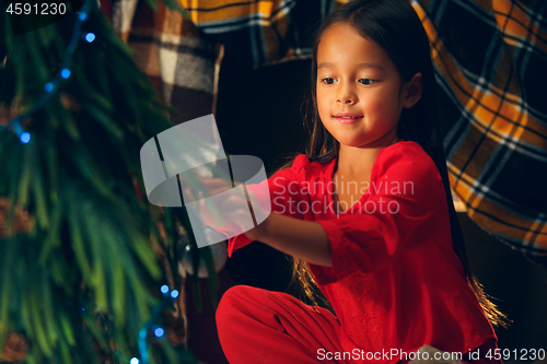 Image of christmas, holidays and childhood concept - happy girl in red clothes decorating natural fir tree
