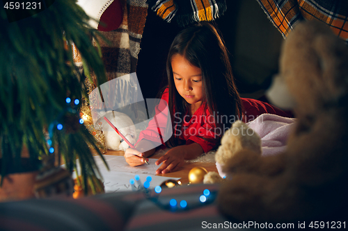 Image of Merry Christmas and Happy Holidays. Cute little child girl writes the letter to Santa Claus near Christmas tree