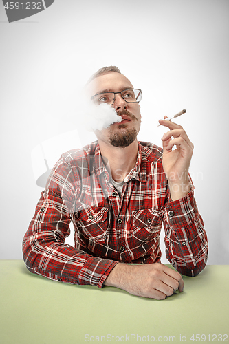 Image of Handsome hipster man smoking cigarette at home. Man looking upwards and enjoying spending free time.