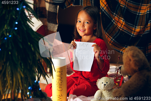 Image of Merry Christmas and Happy Holidays. Cute little child girl writes the letter to Santa Claus near Christmas tree