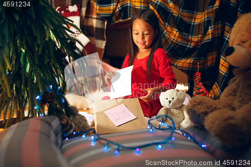 Image of Merry Christmas and Happy Holidays. Cute little child girl writes the letter to Santa Claus near Christmas tree