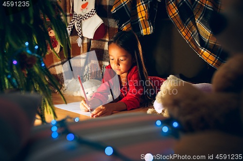 Image of Merry Christmas and Happy Holidays. Cute little child girl writes the letter to Santa Claus near Christmas tree