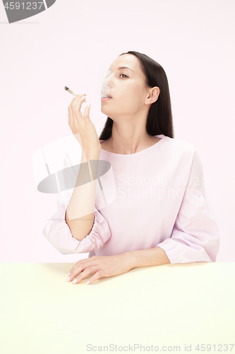 Image of Handsome young women smoking while sitting at table at studio. Trendy colors