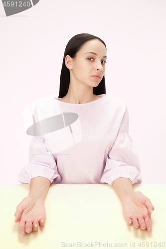 Image of Serious business woman sitting at a table on a pink background