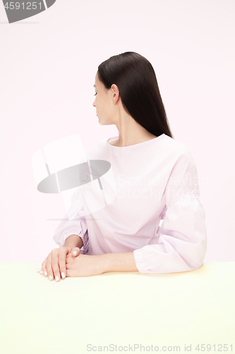 Image of Serious business woman sitting at a table on a pink background