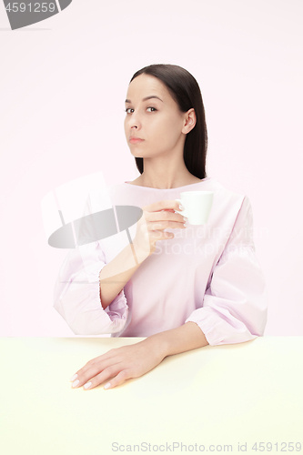 Image of Beautiful lonely woman sitting at studio and looking sad holding the cup of coffee in hand. Closeup toned portrait