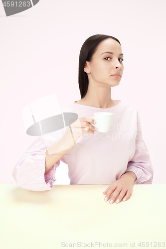 Image of Beautiful lonely woman sitting at studio and looking sad holding the cup of coffee in hand. Closeup toned portrait