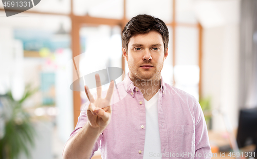 Image of young man showing three fingers over office