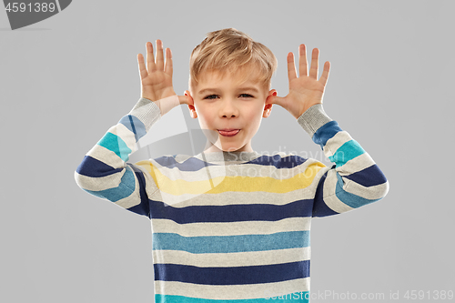 Image of little boy in red t-shirt making big ears by hands