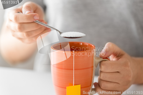 Image of close up of woman adding sugar to cup of tea