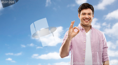 Image of smiling young man showing ok hand sign over sky