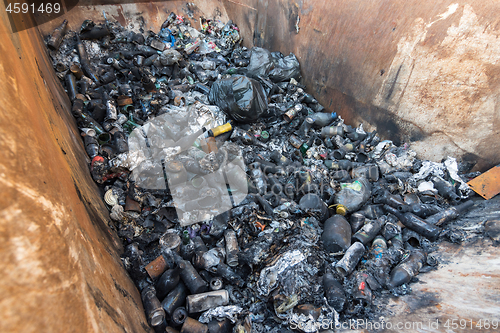 Image of In a large garbage tank lie charred glass and allumines and bottles