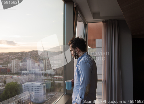 Image of young man enjoying evening coffee by the window