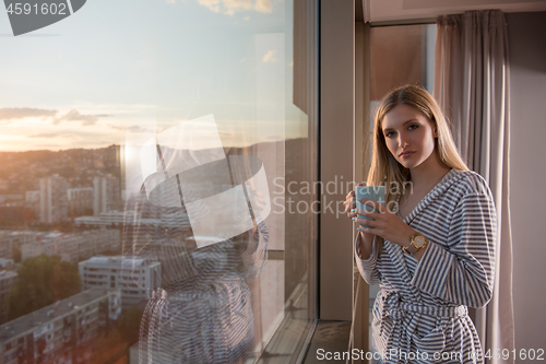 Image of young woman enjoying evening coffee by the window