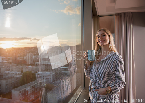 Image of young woman enjoying evening coffee by the window