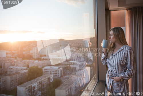 Image of young woman enjoying evening coffee by the window