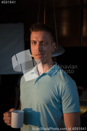 Image of young man enjoying evening coffee by the window