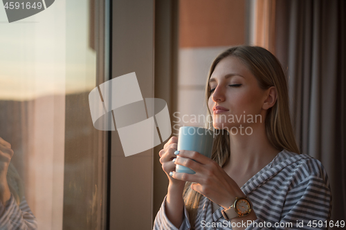 Image of young woman enjoying evening coffee by the window