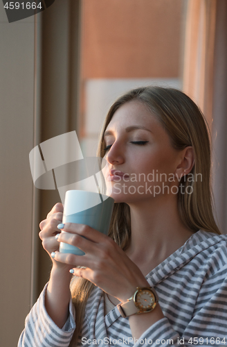 Image of young woman enjoying evening coffee by the window