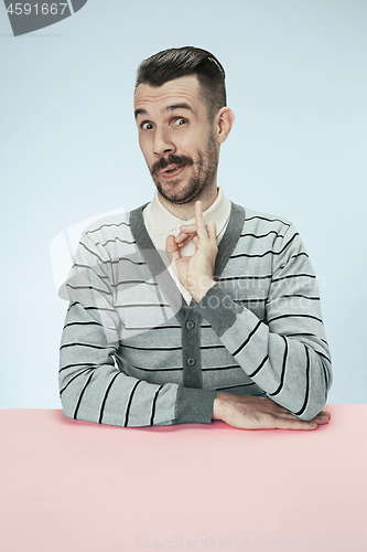 Image of The happy smiling businessman sitting at a table on a blue background