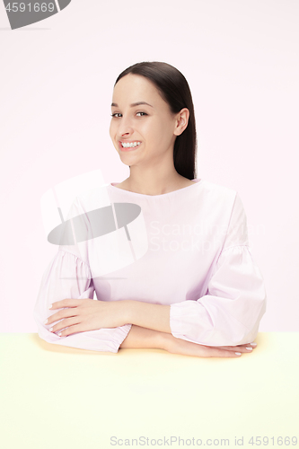 Image of The happy and smiling business woman sitting at a table on a pink background