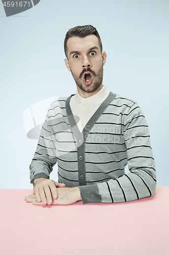 Image of Surprised business man sitting at a table on a blue background