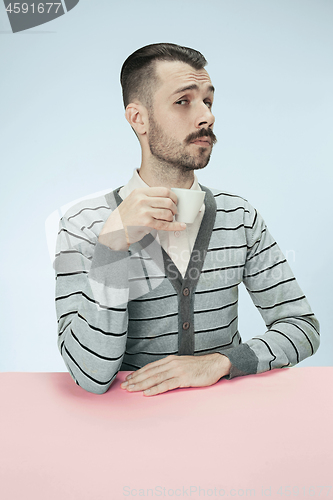 Image of lonely man sitting at studio and looking sad holding the cup of coffee in hand. Closeup toned portrait