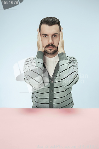 Image of portrait of stressed man sitting at table with closed and covering her ears with hands.