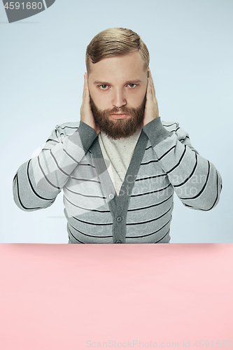 Image of portrait of stressed man sitting at table with closed and covering her ears with hands.