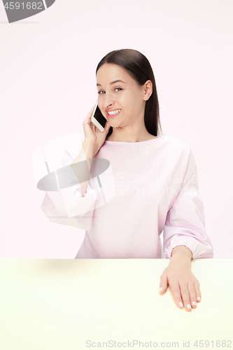 Image of The happy business woman sitting with mobile phone against pink background.