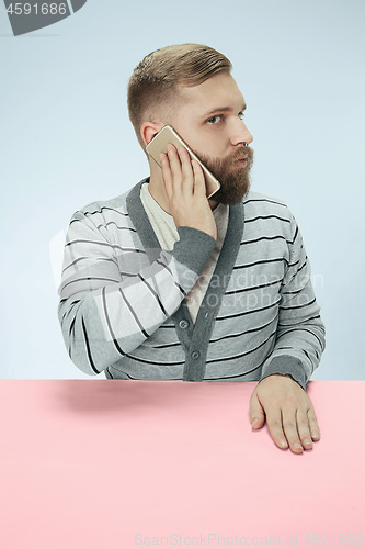 Image of Surprised business man talking on phone sitting at the table