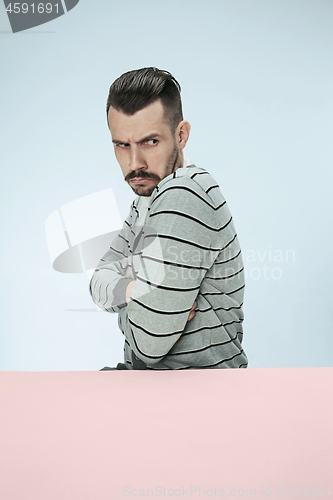 Image of Serious suspicious business man sitting at a table on a blue background