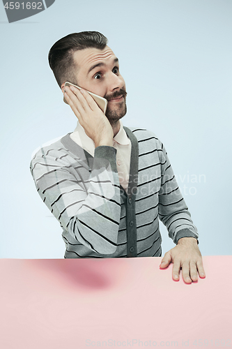 Image of Surprised business man talking on phone sitting at the table