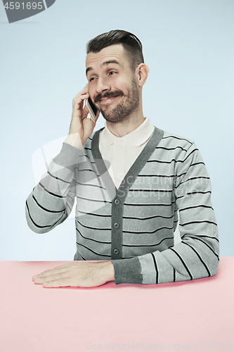 Image of Smiling happy business man talking on phone sitting at the table