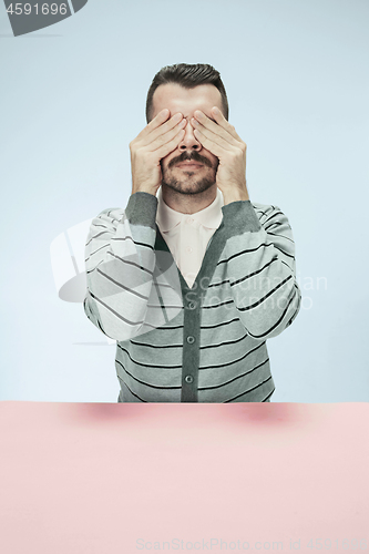 Image of Young man sitting at table at studio with eyes closed isolated on blue