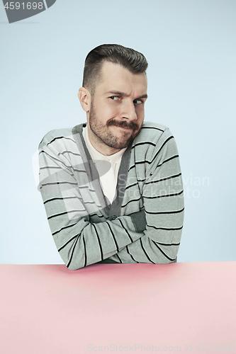 Image of Serious suspicious business man sitting at a table on a blue background