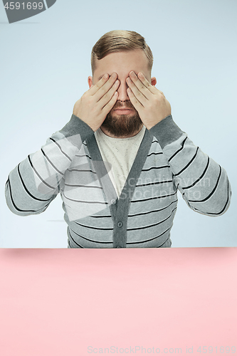 Image of Young man sitting at table at studio with eyes closed isolated on blue