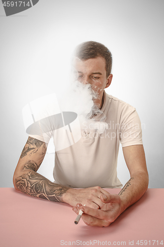 Image of Handsome hipster man smoking cigarette at home. Man looking upwards and enjoying spending free time.