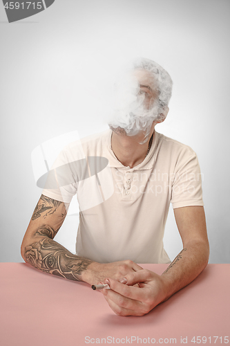 Image of Handsome hipster man smoking cigarette at home. Man looking upwards and enjoying spending free time.