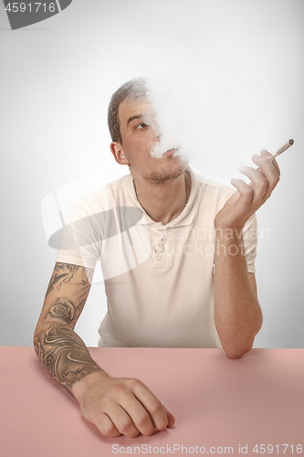 Image of Handsome hipster man smoking cigarette at home. Man looking upwards and enjoying spending free time.