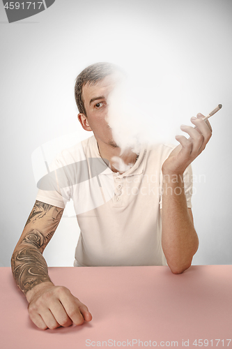 Image of Handsome hipster man smoking cigarette at home. Man looking upwards and enjoying spending free time.