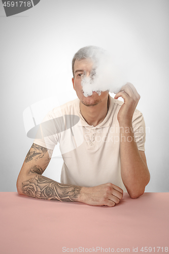 Image of Handsome hipster man smoking cigarette at home. Man looking upwards and enjoying spending free time.