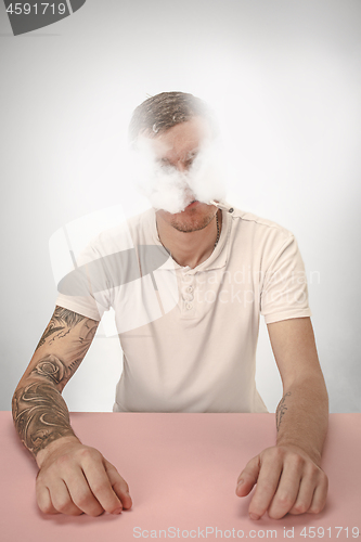 Image of Handsome hipster man smoking cigarette at home. Man looking upwards and enjoying spending free time.