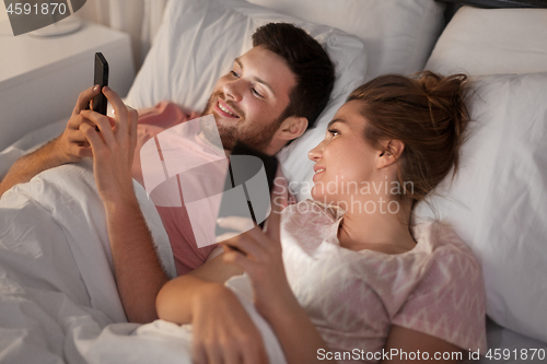 Image of happy couple using smartphones in bed at night