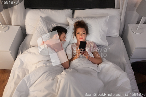 Image of woman using smartphone while boyfriend is sleeping