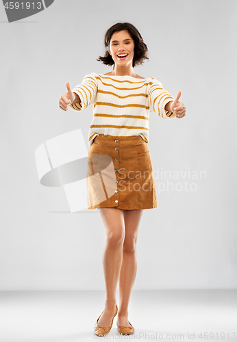 Image of woman in pullover, skirt and shoes shows thumbs up