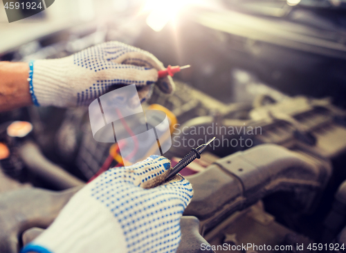 Image of auto mechanic man with multimeter testing battery