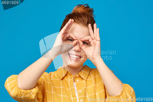 Image of red haired teenage girl making finger glasses